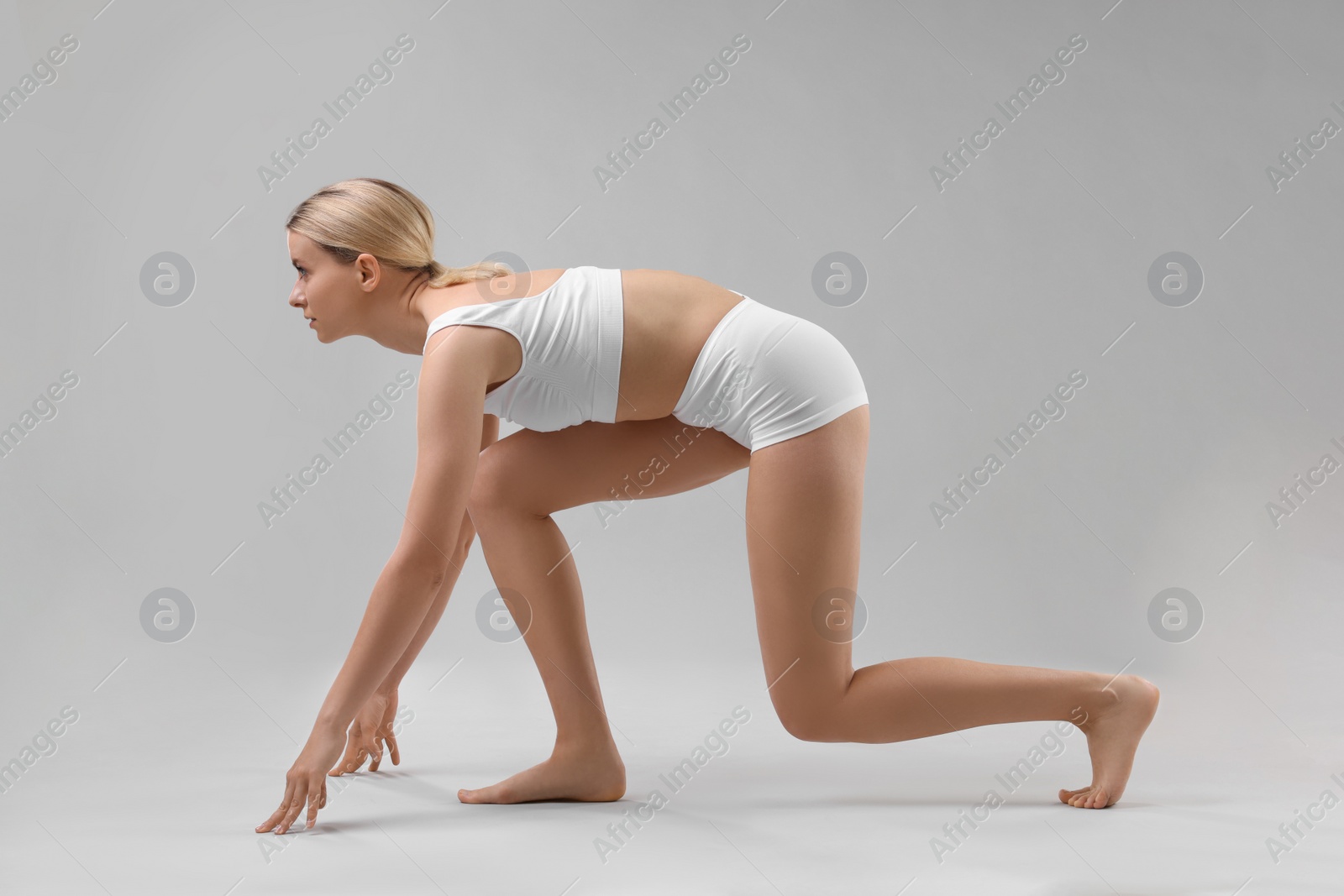 Photo of Sporty woman in starting position for run on grey background