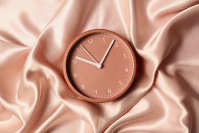 Photo of One stylish clock on beige cloth, top view