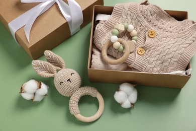Different baby accessories, knitted clothes and cotton flowers on green background, above view