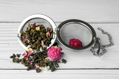 Snap infuser with dried herbal tea leaves and flowers on white wooden table, closeup