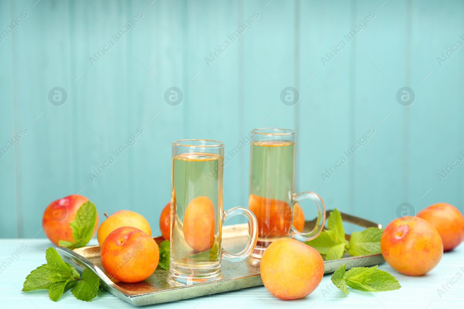 Photo of Delicious plum liquor, ripe fruits and mint on table against light blue background, space for text. Homemade strong alcoholic beverage