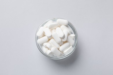 Photo of Vitamin capsules in bowl on light grey background, top view