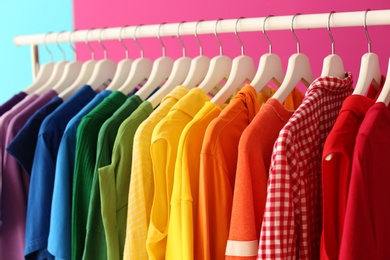 Photo of Rack with rainbow clothes on color background