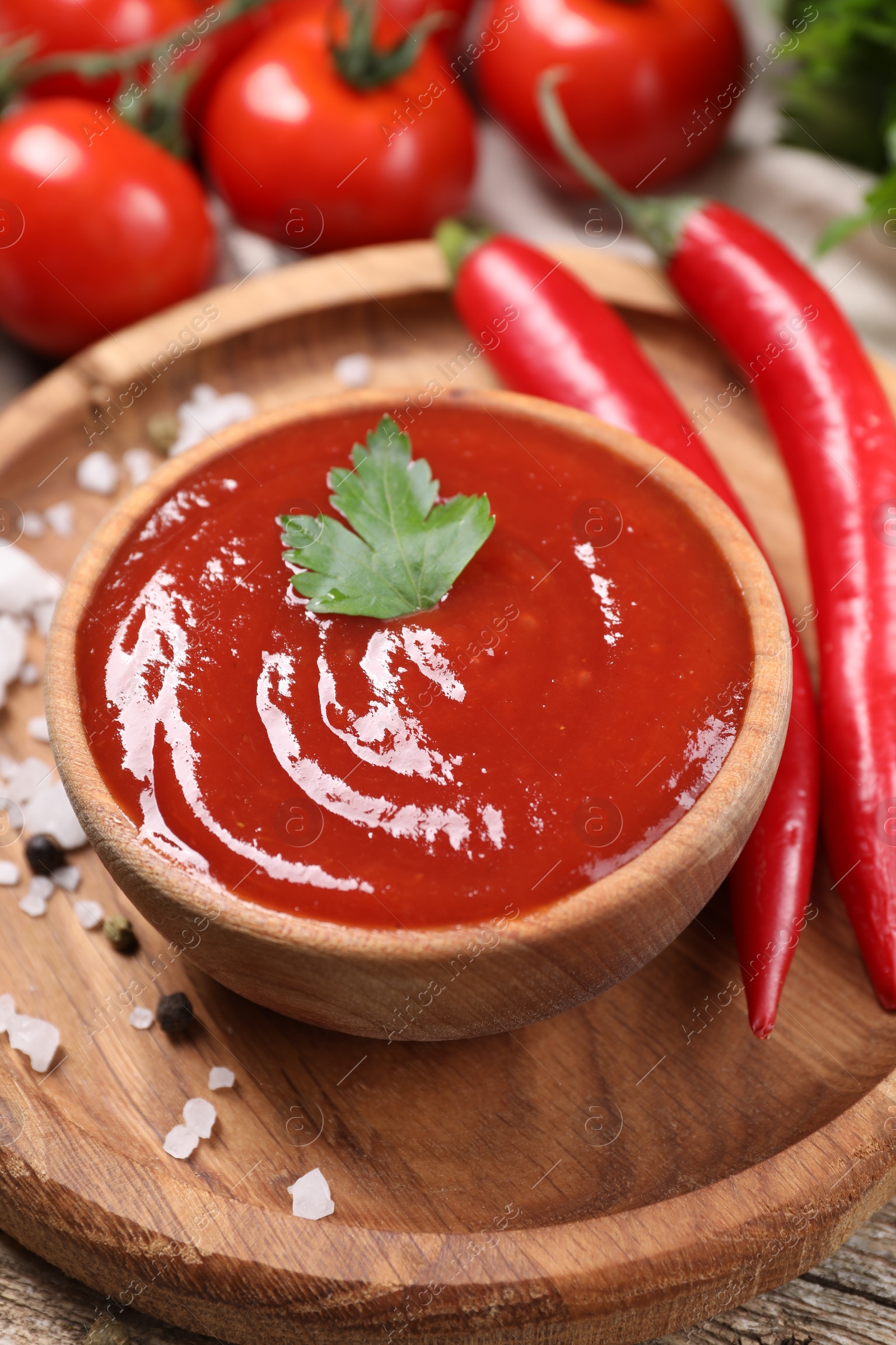 Photo of Delicious ketchup in bowl and spices on wooden table, closeup. Tomato sauce