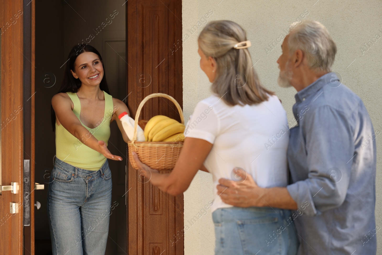 Photo of Friendly relationship with neighbours. Elderly couple with wicker basket of products treating young woman outdoors