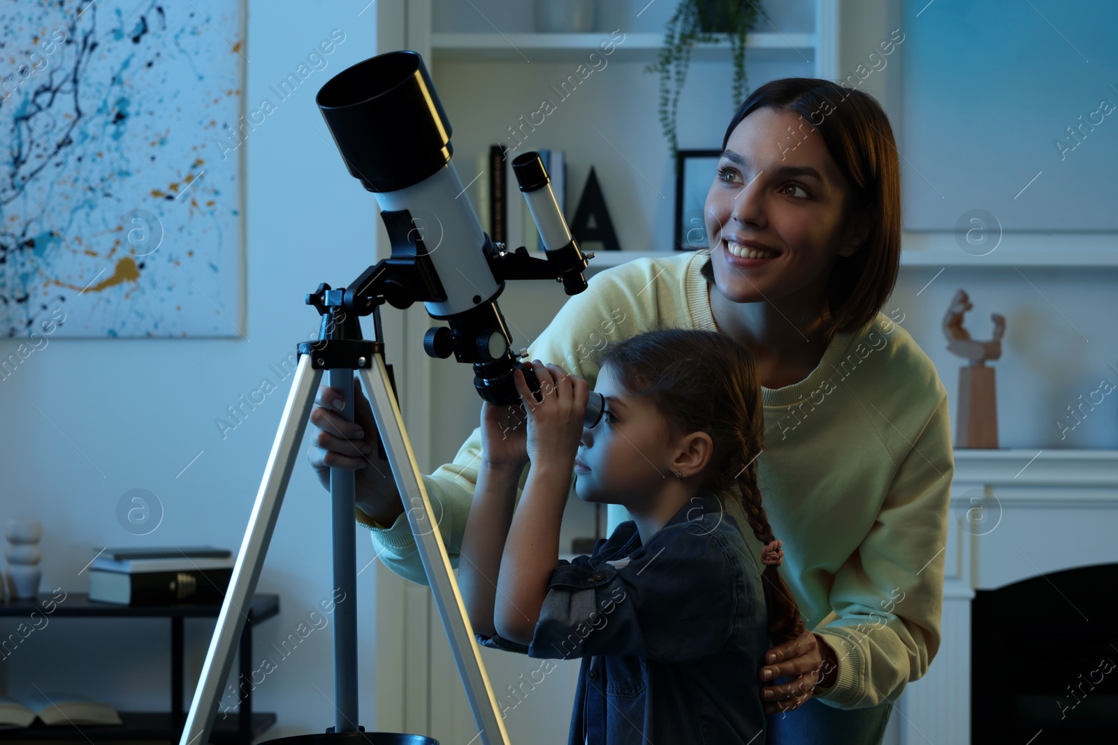 Photo of Happy mother and her cute daughter looking at stars through telescope in room