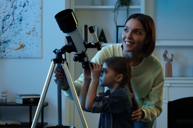 Photo of Happy mother and her cute daughter looking at stars through telescope in room