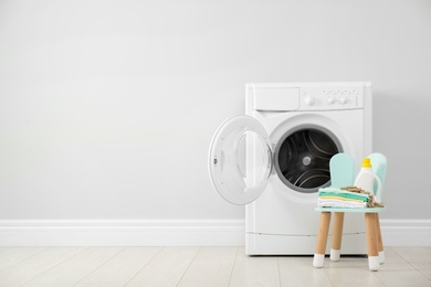 Photo of Bottle of detergent and children's clothes on chair near washing machine. Space for text