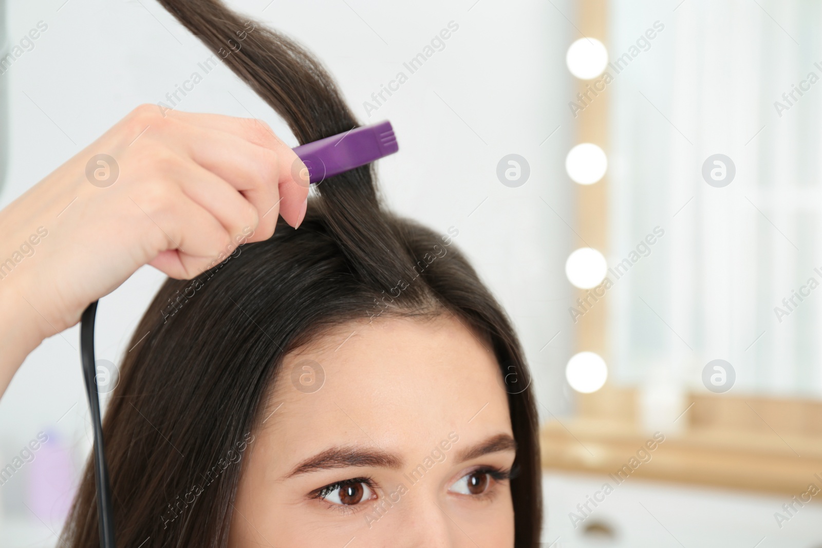 Photo of Hairdresser using modern flat iron to style client's hair in salon, closeup. Space for text