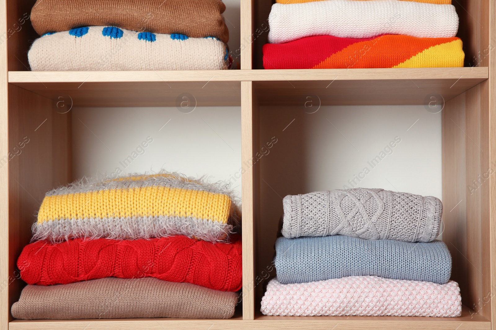 Photo of Stacks of folded winter clothes on shelves in wardrobe