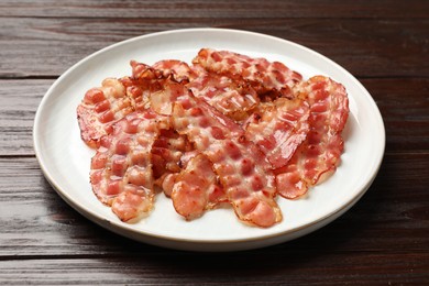 Photo of Plate with fried bacon slices on wooden table, closeup