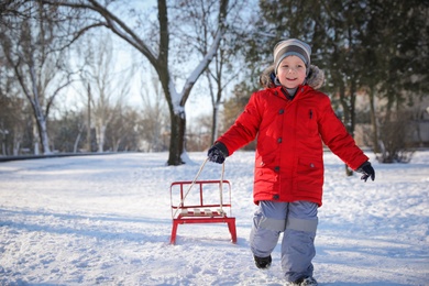Photo of Cute little boy with sleigh in snowy park