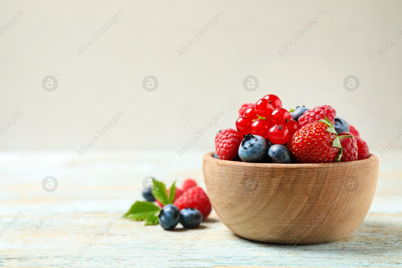 Photo of Mix of different fresh berries in bowl on wooden table. Space for text