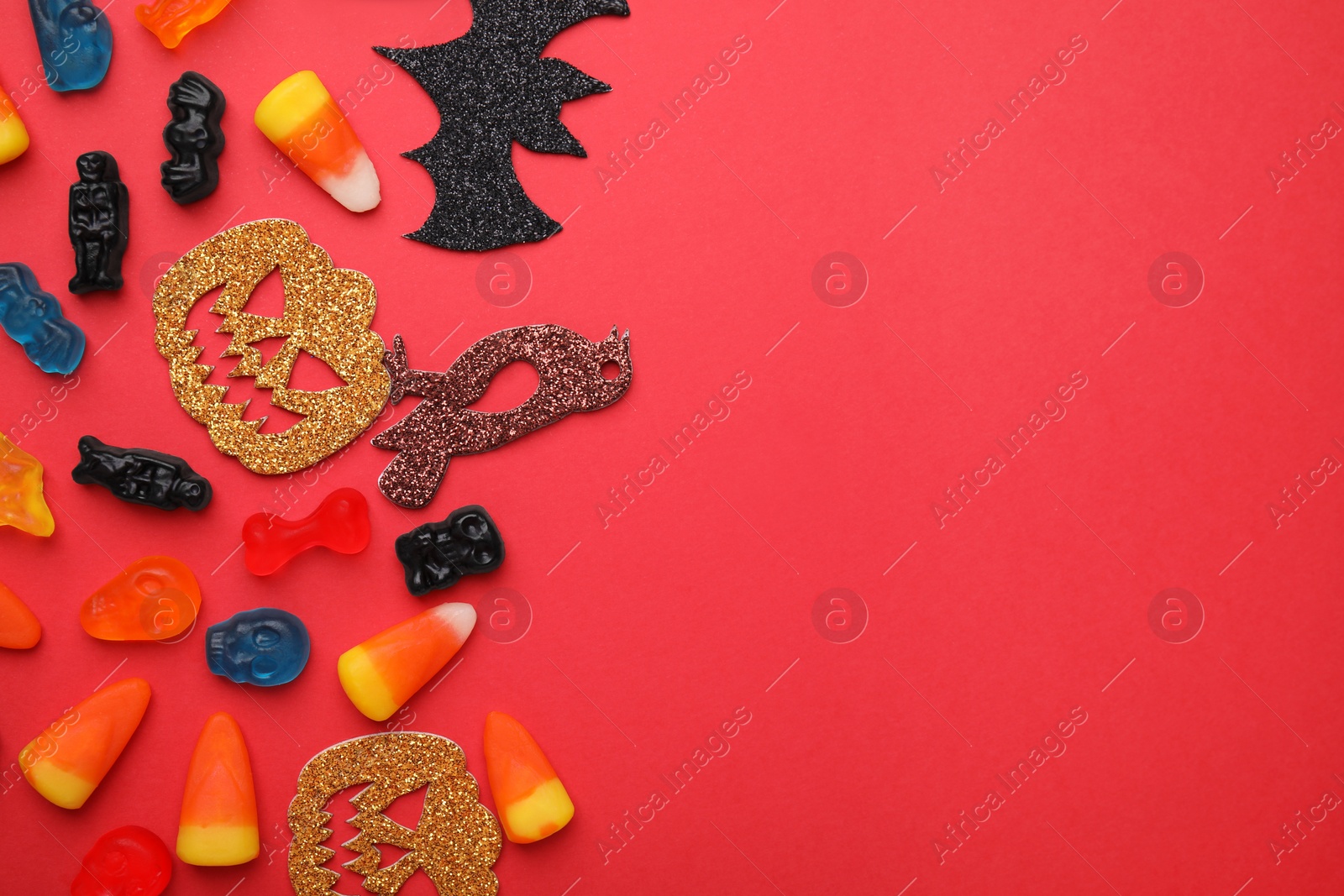 Photo of Tasty candies and Halloween decorations on red background, flat lay. Space for text