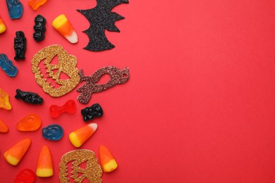 Photo of Tasty candies and Halloween decorations on red background, flat lay. Space for text