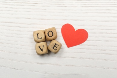 Photo of Mini cubes with letters forming word Love near red paper heart on white wooden background, flat lay