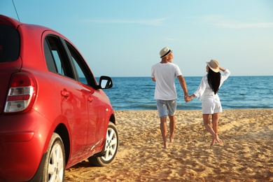 Photo of Happy couple walking on sandy beach, back view. Summer trip