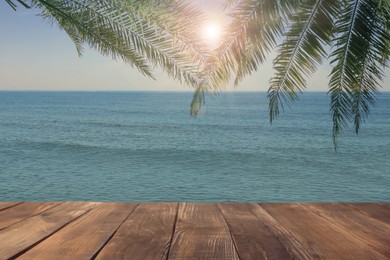 Image of Wooden table under green palm leaves near ocean on sunny day