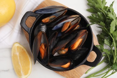 Photo of Pan of cooked mussels with parsley and lemon on white marble table, flat lay