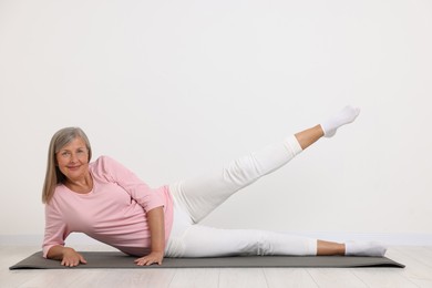 Photo of Happy senior woman practicing yoga on mat near white wall
