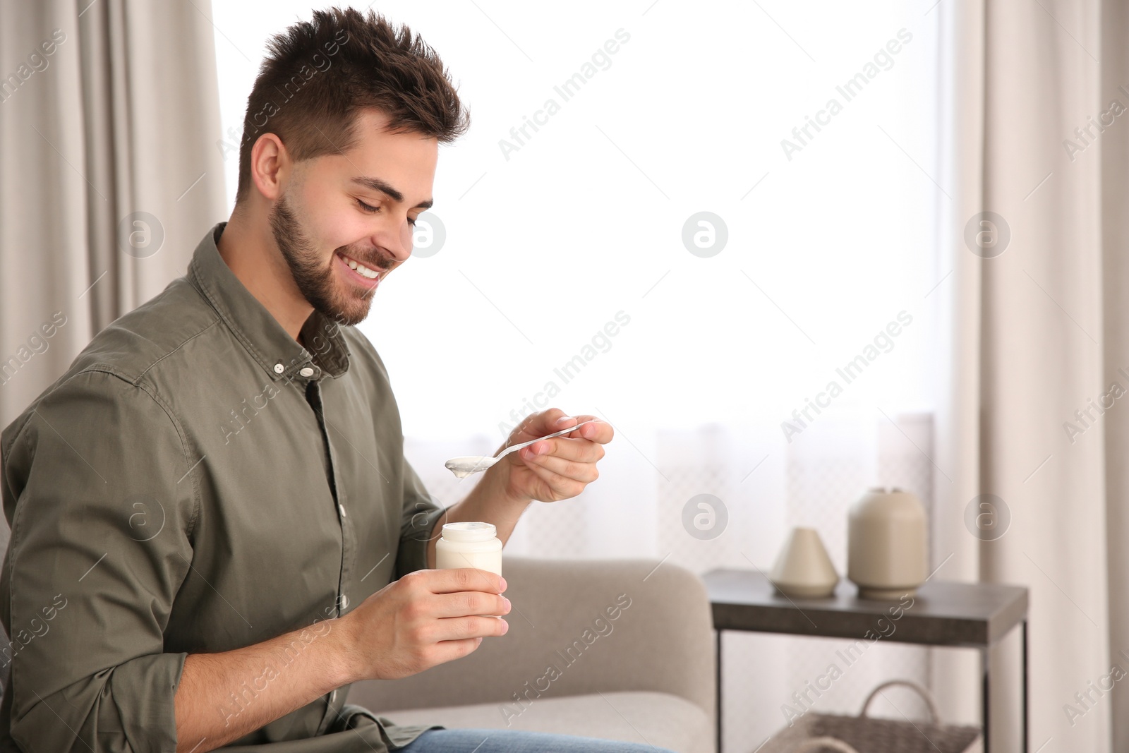 Photo of Happy young man with tasty yogurt in living room. Space for text