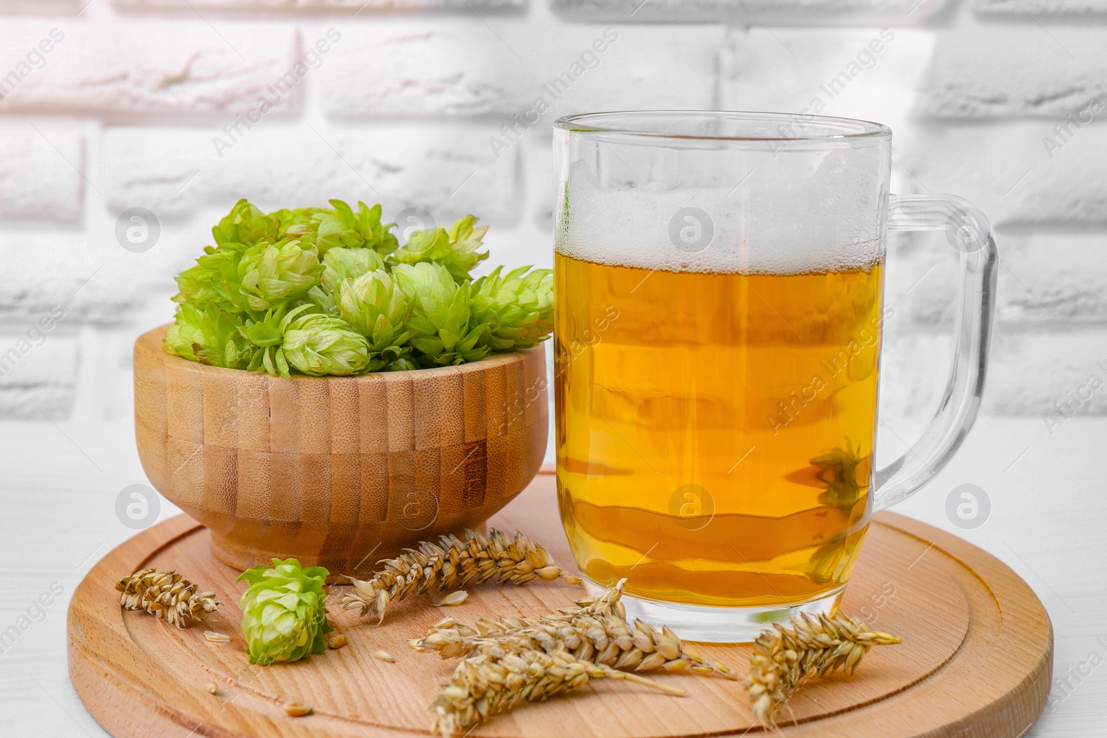 Photo of Mug with beer, fresh hops and ears of wheat on white wooden table