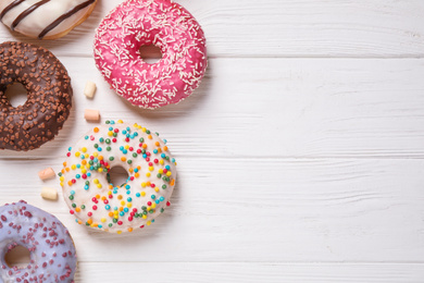 Photo of Yummy donuts and space for text on white wooden background, flat lay