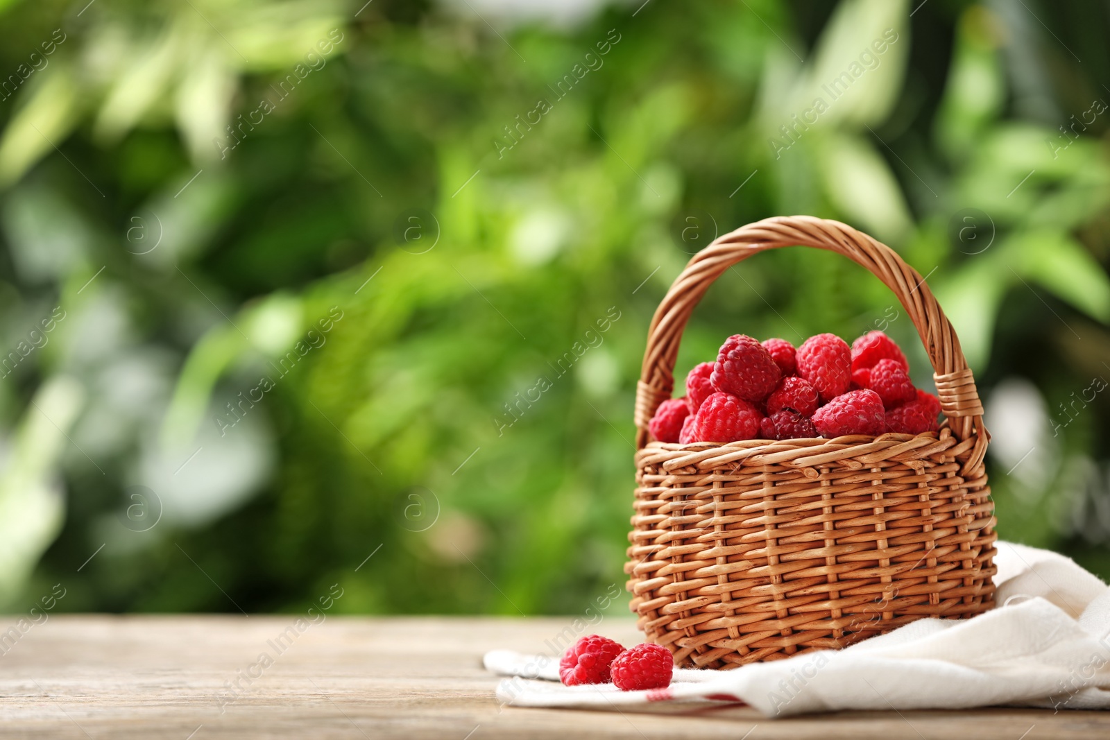 Photo of Wicker basket with delicious ripe raspberries on wooden table against blurred background, space for text