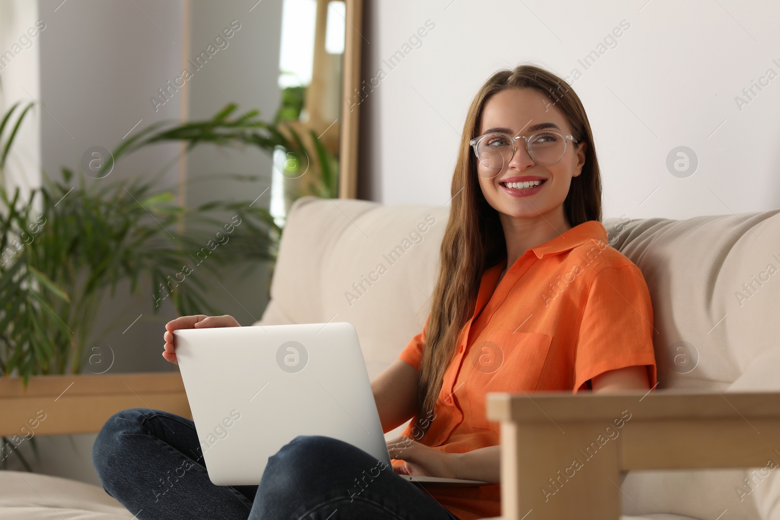 Photo of Happy young woman with laptop on sofa at home