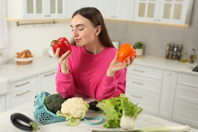 Woman with peppers and string bag of vegetables at light marble table in kitchen