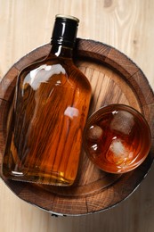 Photo of Wooden barrel, bottle and glass of tasty whiskey on table, top view
