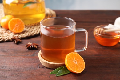 Photo of Cup with hot aromatic tea and fresh orange on wooden table
