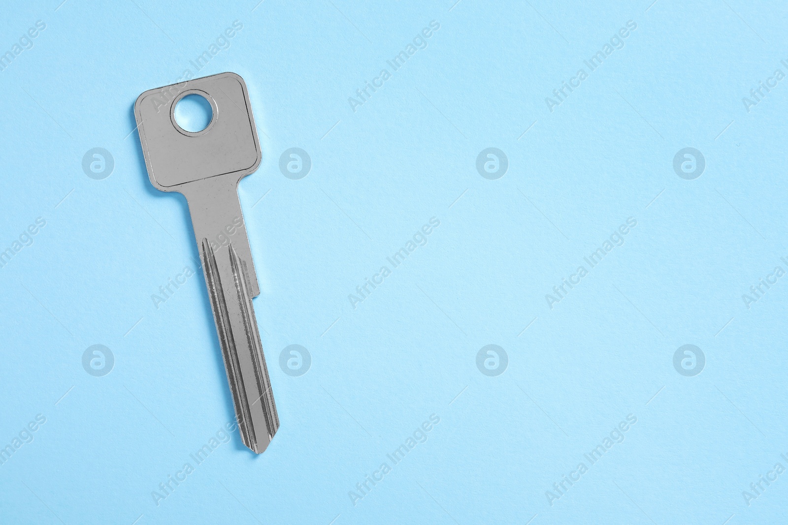 Photo of One key on light blue background, top view. Space for text