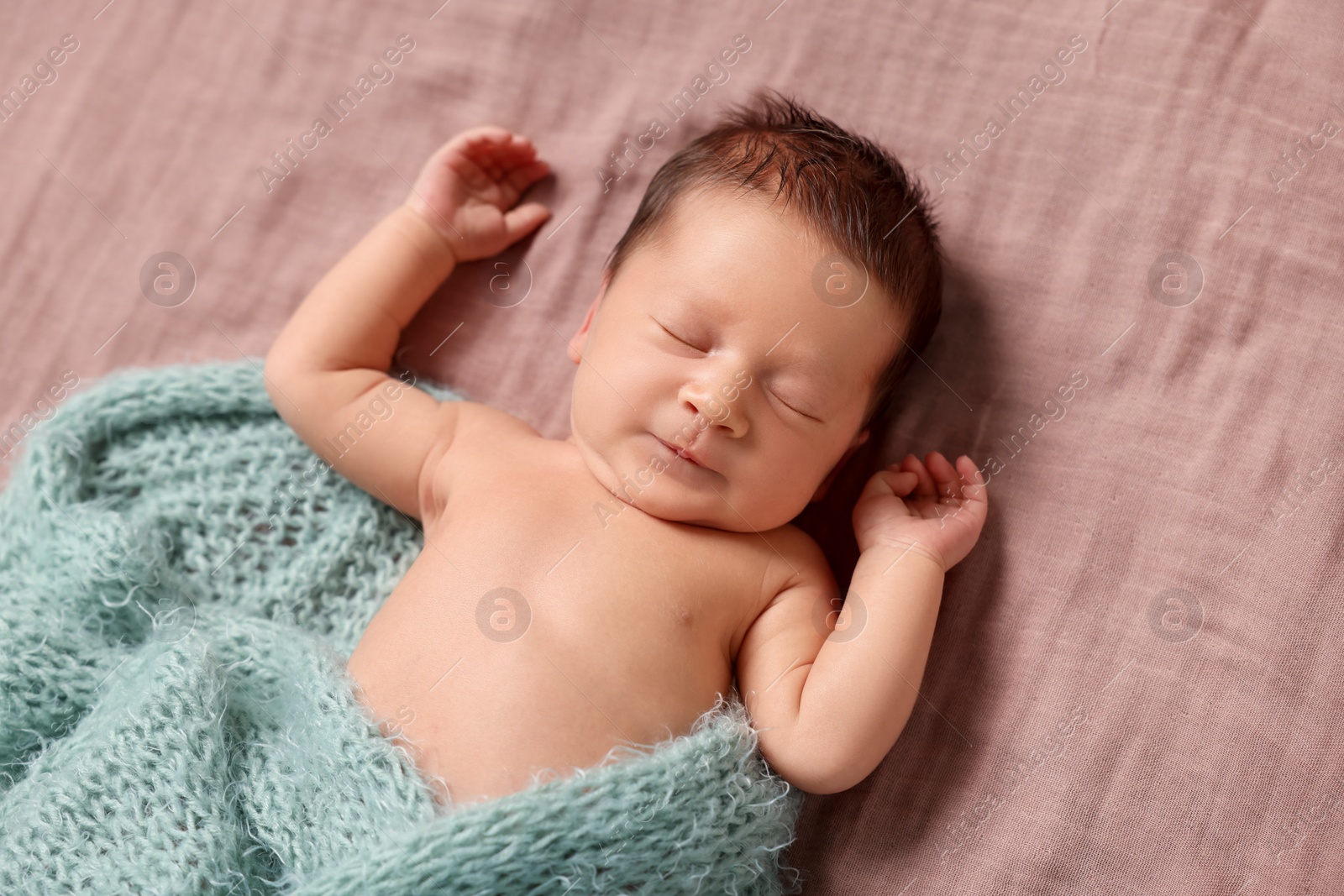 Photo of Adorable newborn baby in turquoise knitted blanket sleeping on bed