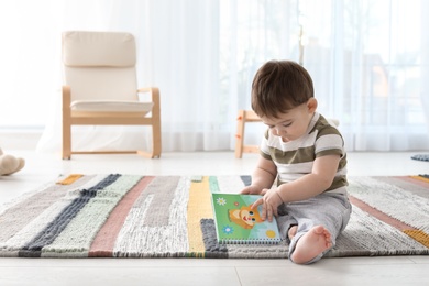 Cute baby sitting on floor with book at home