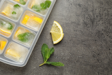 Ice cubes with lemon and mint in tray on grey table, flat lay. Space for text