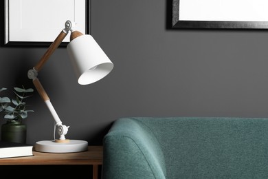 Photo of Stylish modern desk lamp, book and plant on wooden cabinet in living room