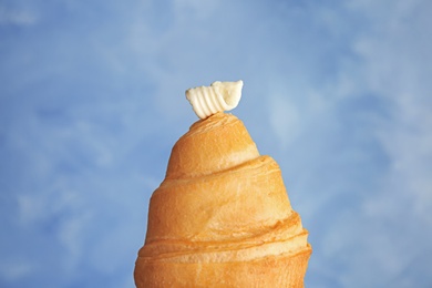 Croissant with tasty butter curl on color background