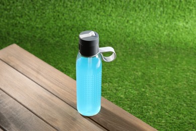 Photo of Light blue drink in bottle on wooden table outdoors