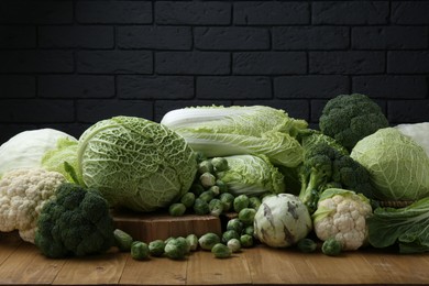 Photo of Many different types of fresh cabbage on wooden table near brick wall