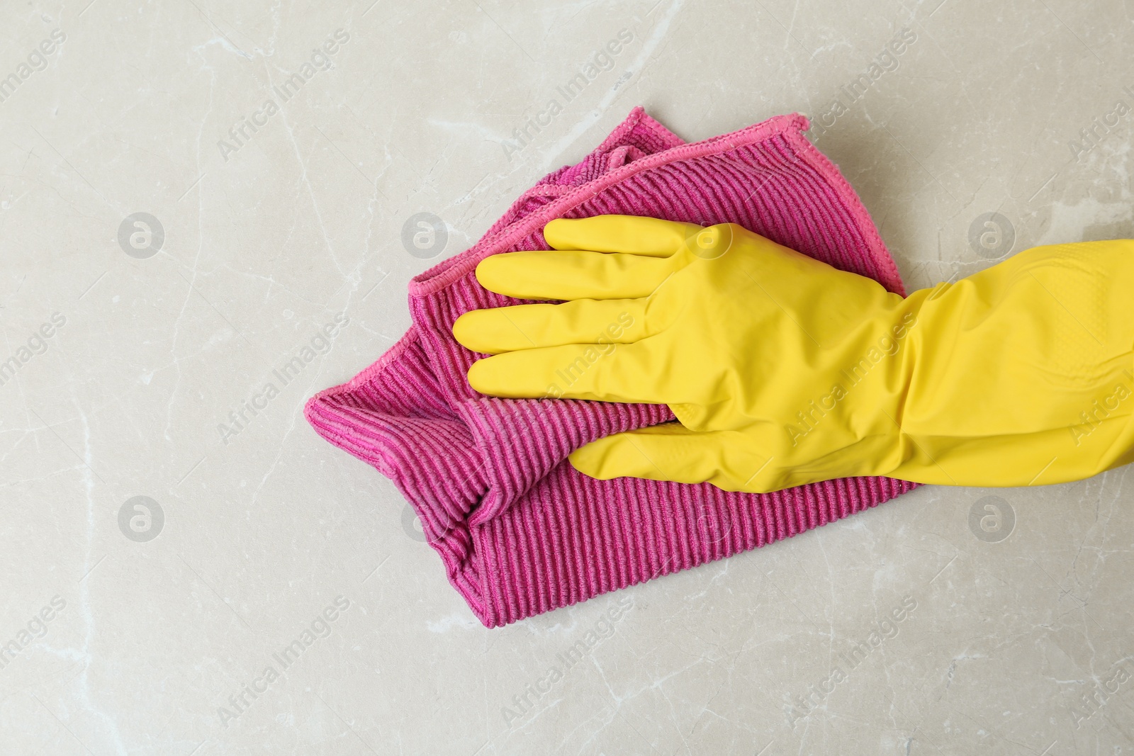 Photo of Person in gloves wiping grey marble table with rag, top view