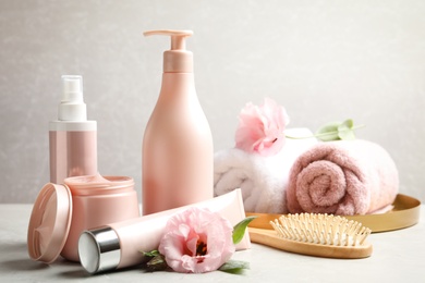 Photo of Set of hair cosmetic products, brush and flowers on  grey table