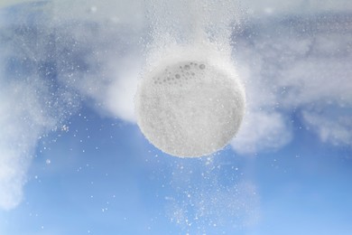 Photo of Effervescent pill dissolving in water on light blue background, closeup