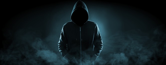 Image of Anonymous man in hood surrounded by smoke on black background. Banner design