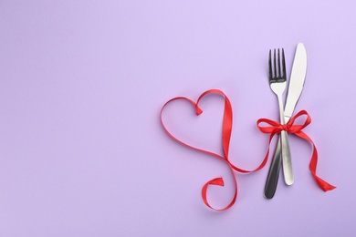 Photo of Beautiful cutlery set and red ribbon on violet background, flat lay with space for text. Valentine's Day dinner
