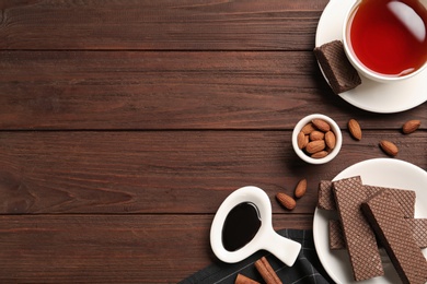 Flat lay composition with delicious chocolate wafers and cup of tea on wooden table. Space for text