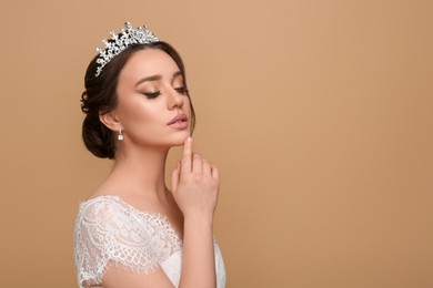 Beautiful young woman wearing luxurious tiara on beige background, space for text