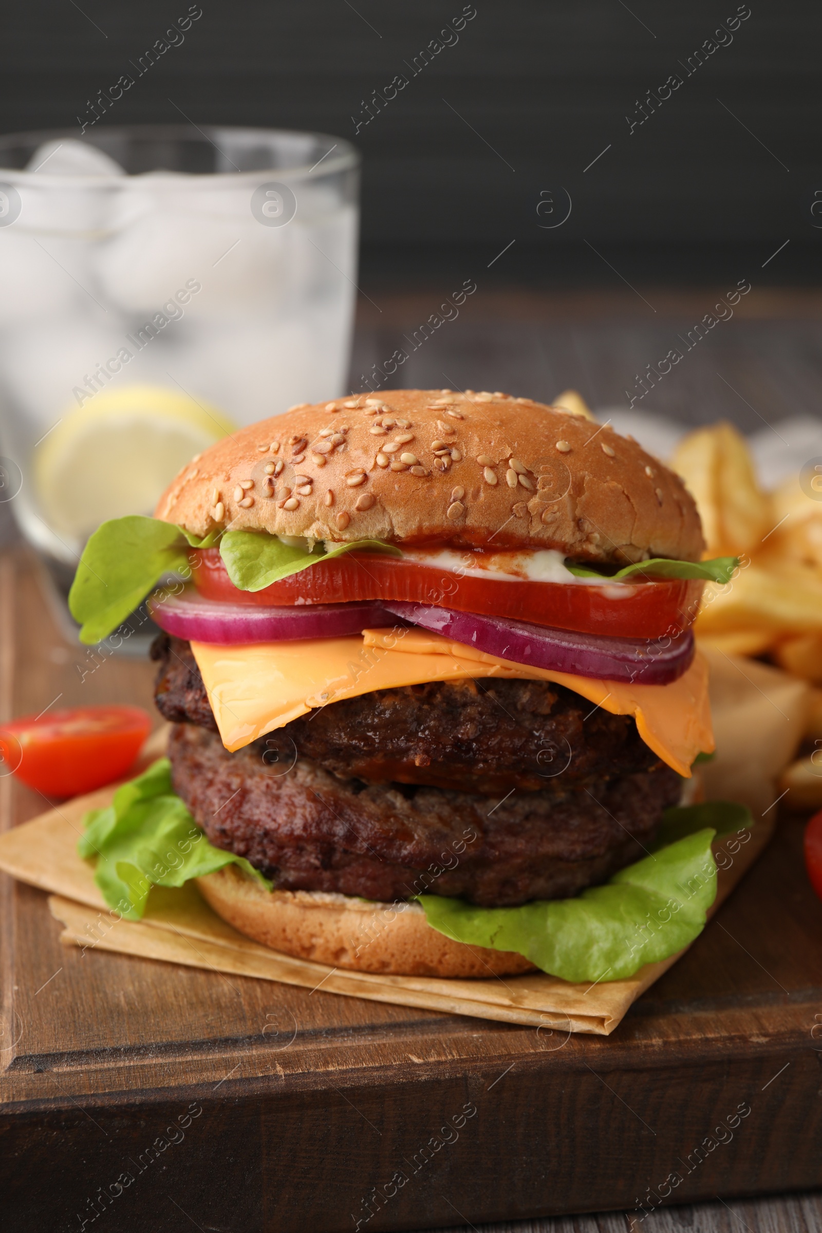Photo of Tasty cheeseburger with patties, onion and tomato on wooden board, closeup
