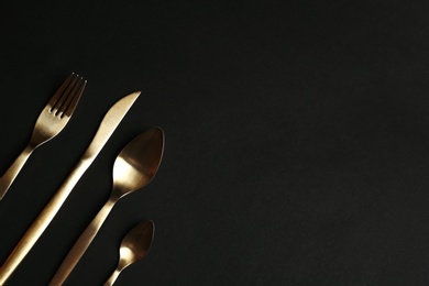 Photo of Set of gold cutlery on black background, flat lay. Space for text