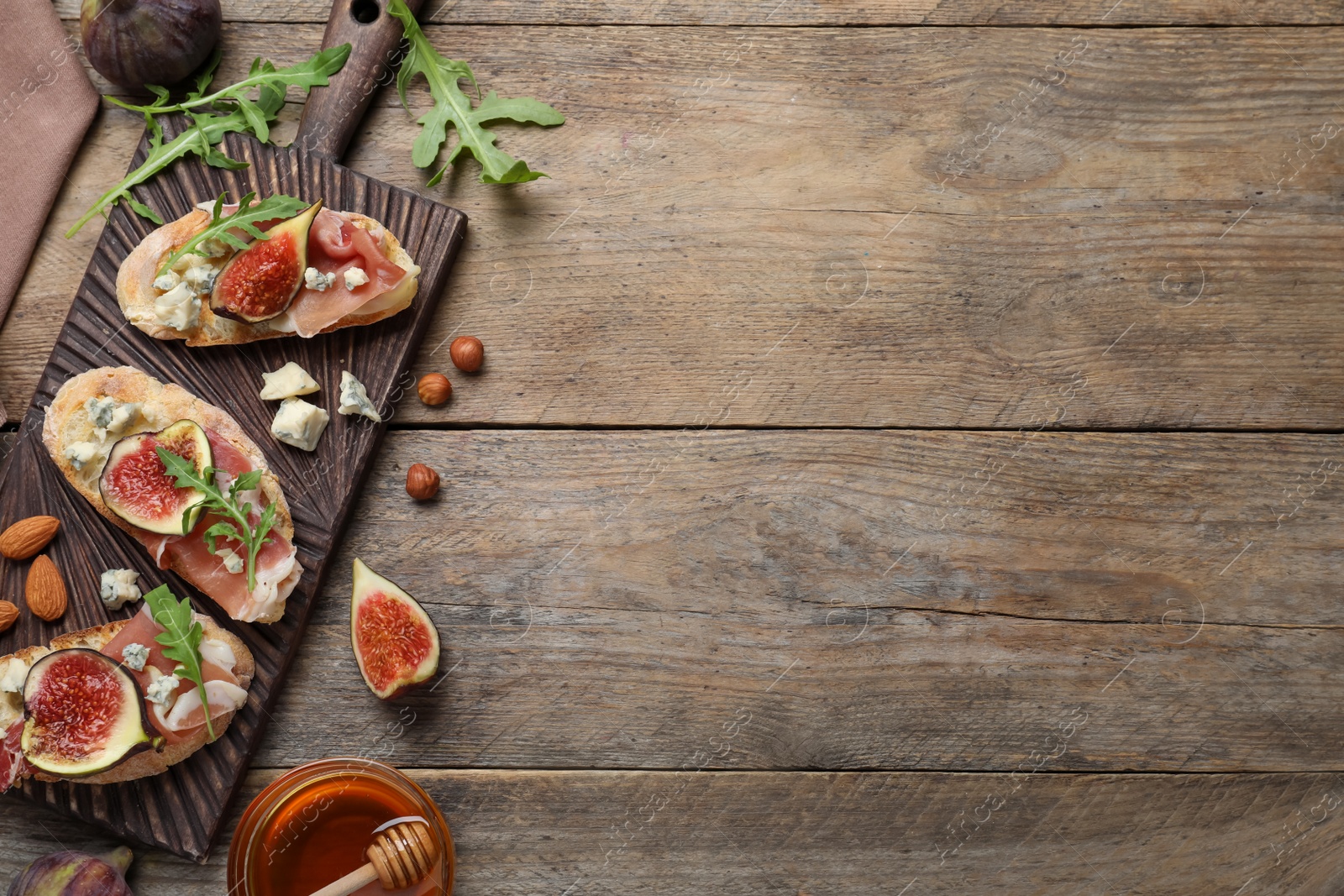 Photo of Sandwiches with ripe figs and prosciutto served on wooden table, flat lay. Space for text